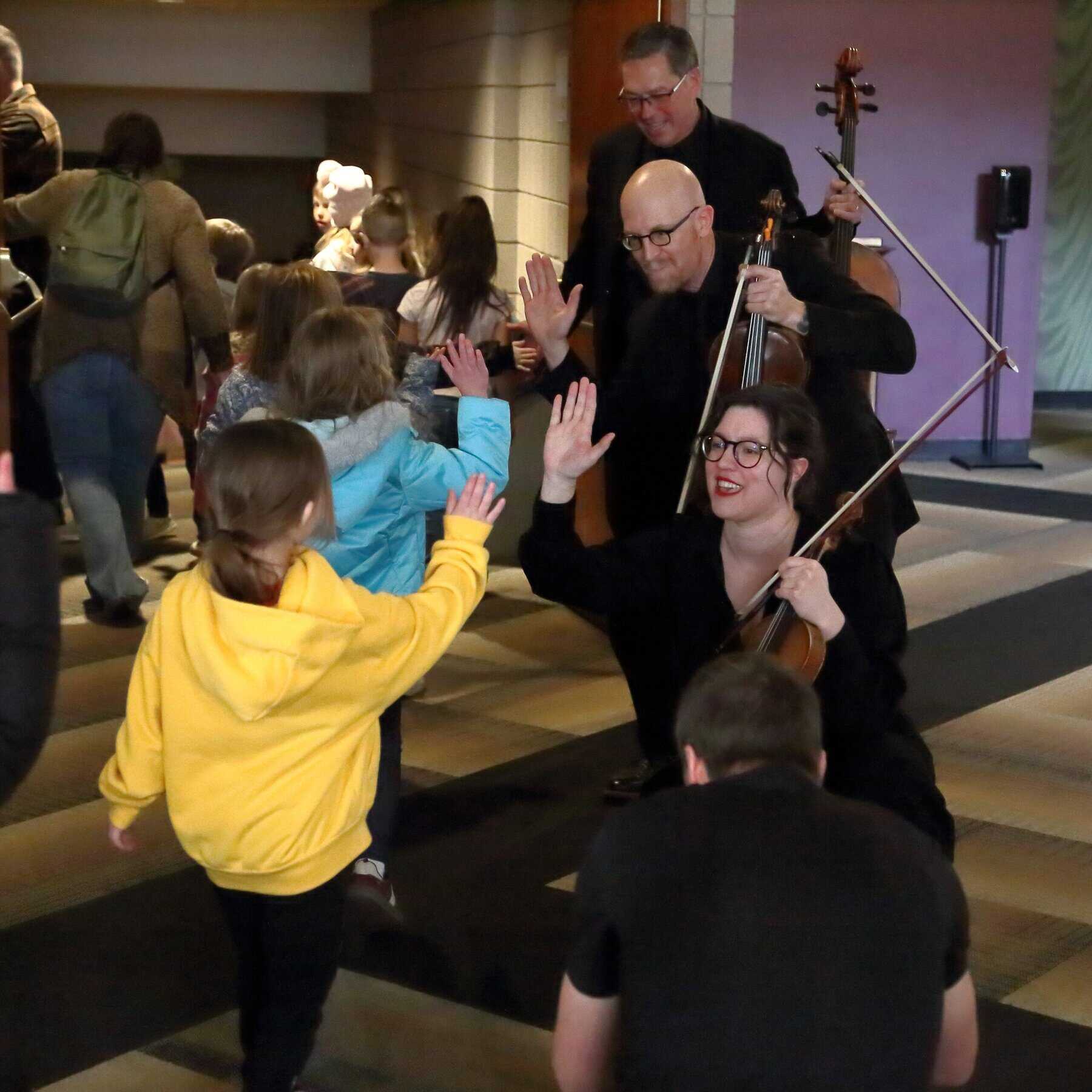Philharmonic musicians high-fiving a line of children
